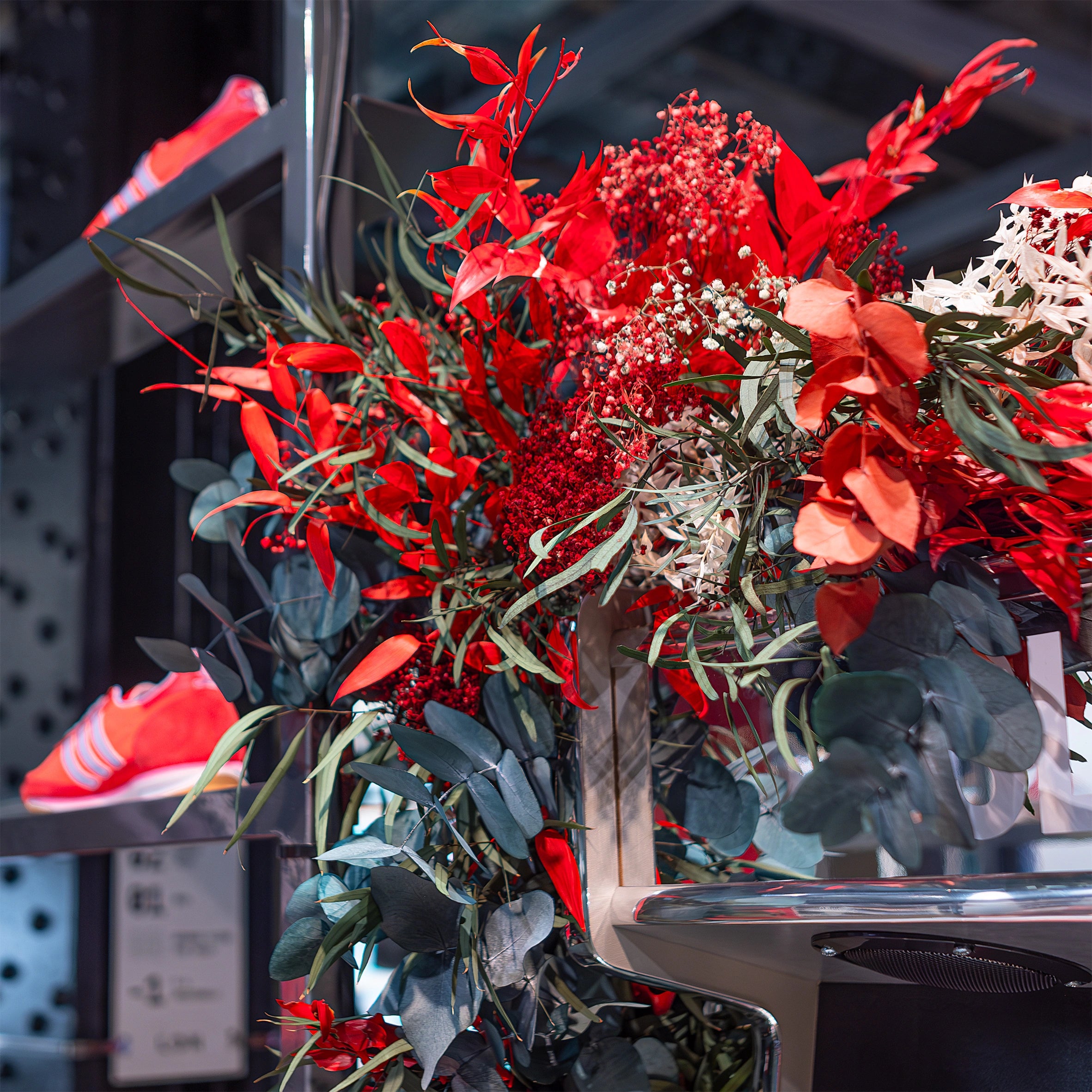 Close-up of a bright red flower arrangement featuring bold red foliage with green leaves at The Adidas Bond Street store. This floral design meets the requirement to accentuate the SL72 collection’s theme with a luxurious, sporty atmosphere.