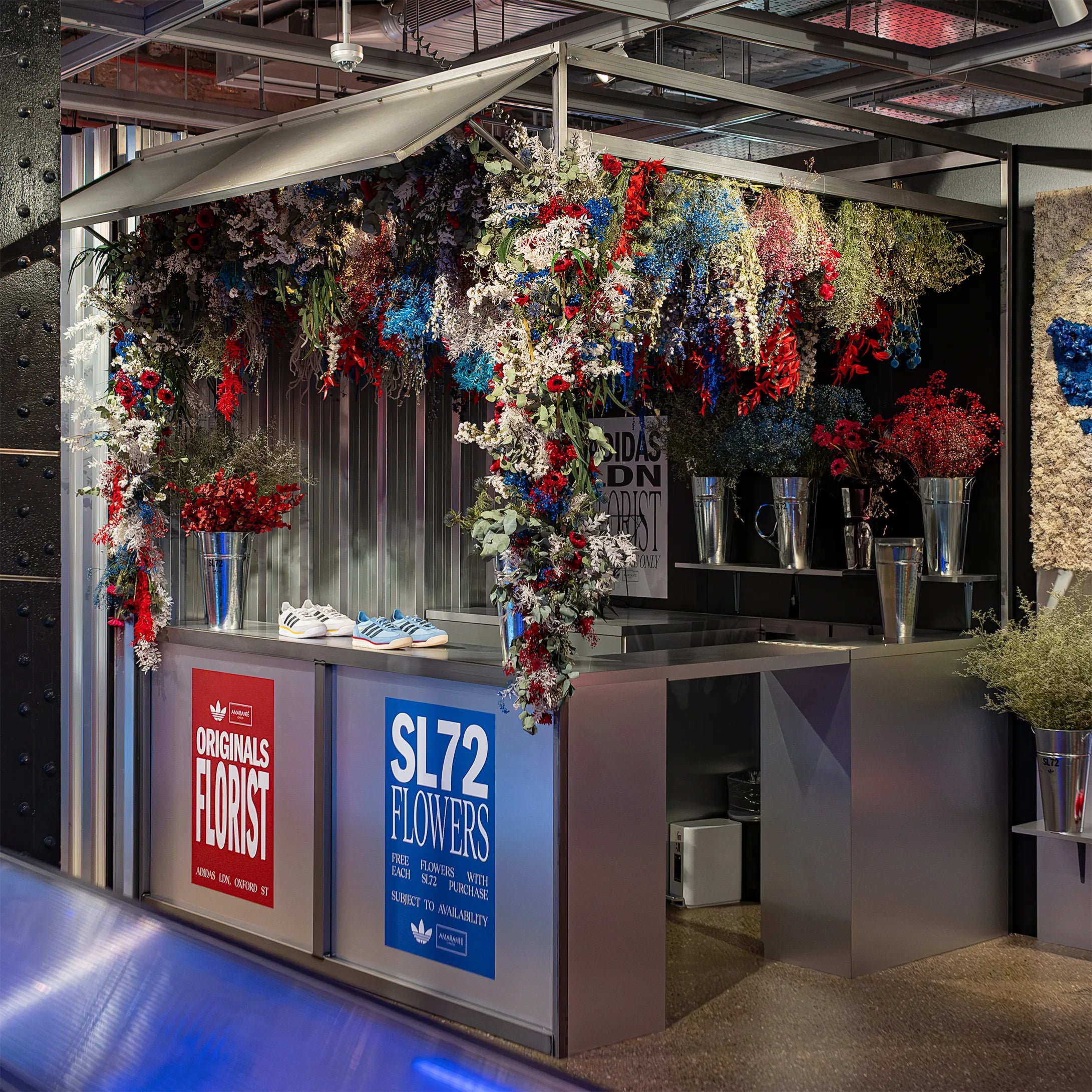 This is another view of the floral ceiling installation display at Adidas' Oxford Street Store, London, for the SL72 collection launch. The vibrant red, white, and blue preserved flowers fill the booth space in the store, providing shoppers with a luxurious and immersive feel - Amaranté London