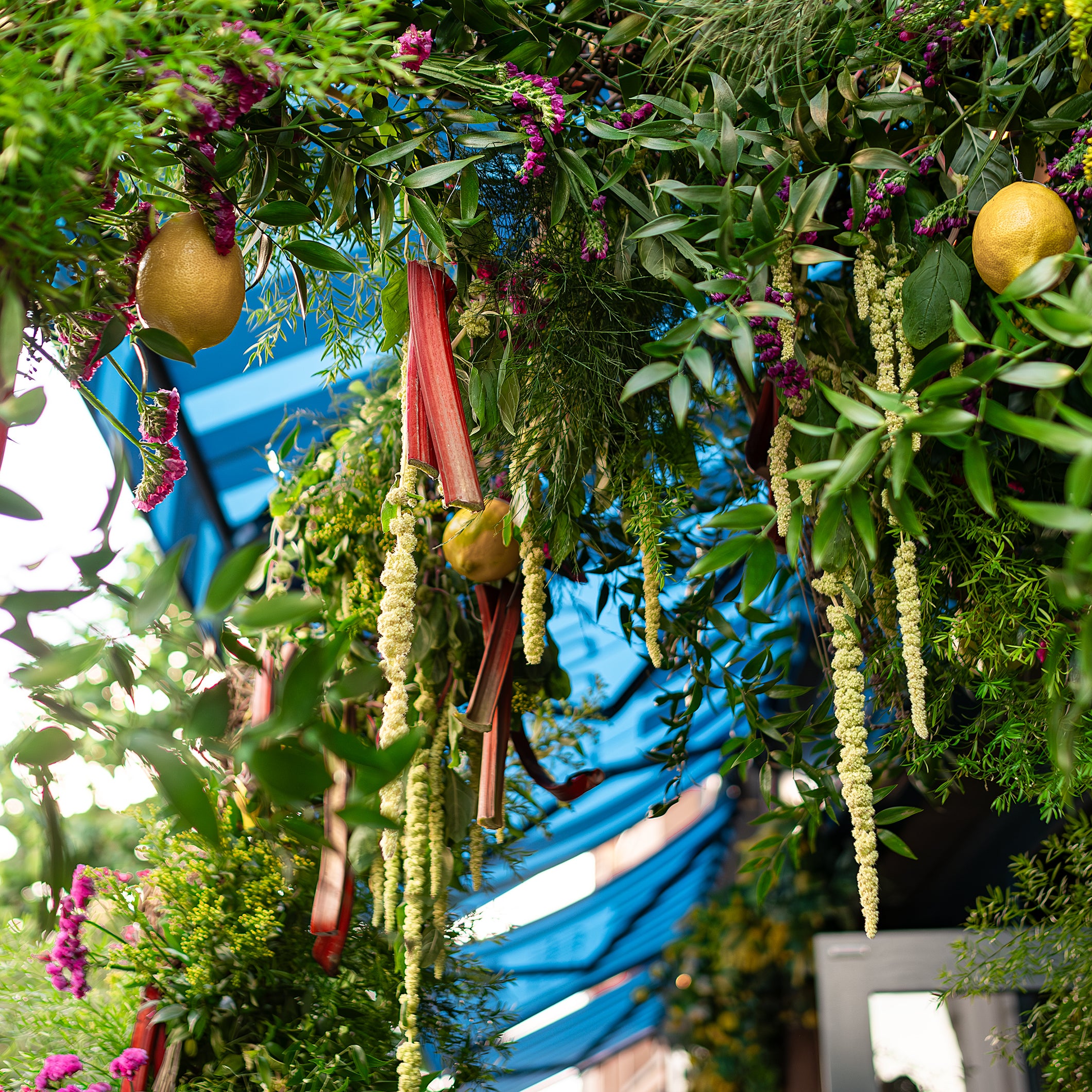 Beautiful floral installation at Chelsea in Bloom, featuring hanging lemons, red stems, and a mix of green foliage and pink flowers, adding a vibrant touch to the entire floral installation - Amaranté London Even Florist
