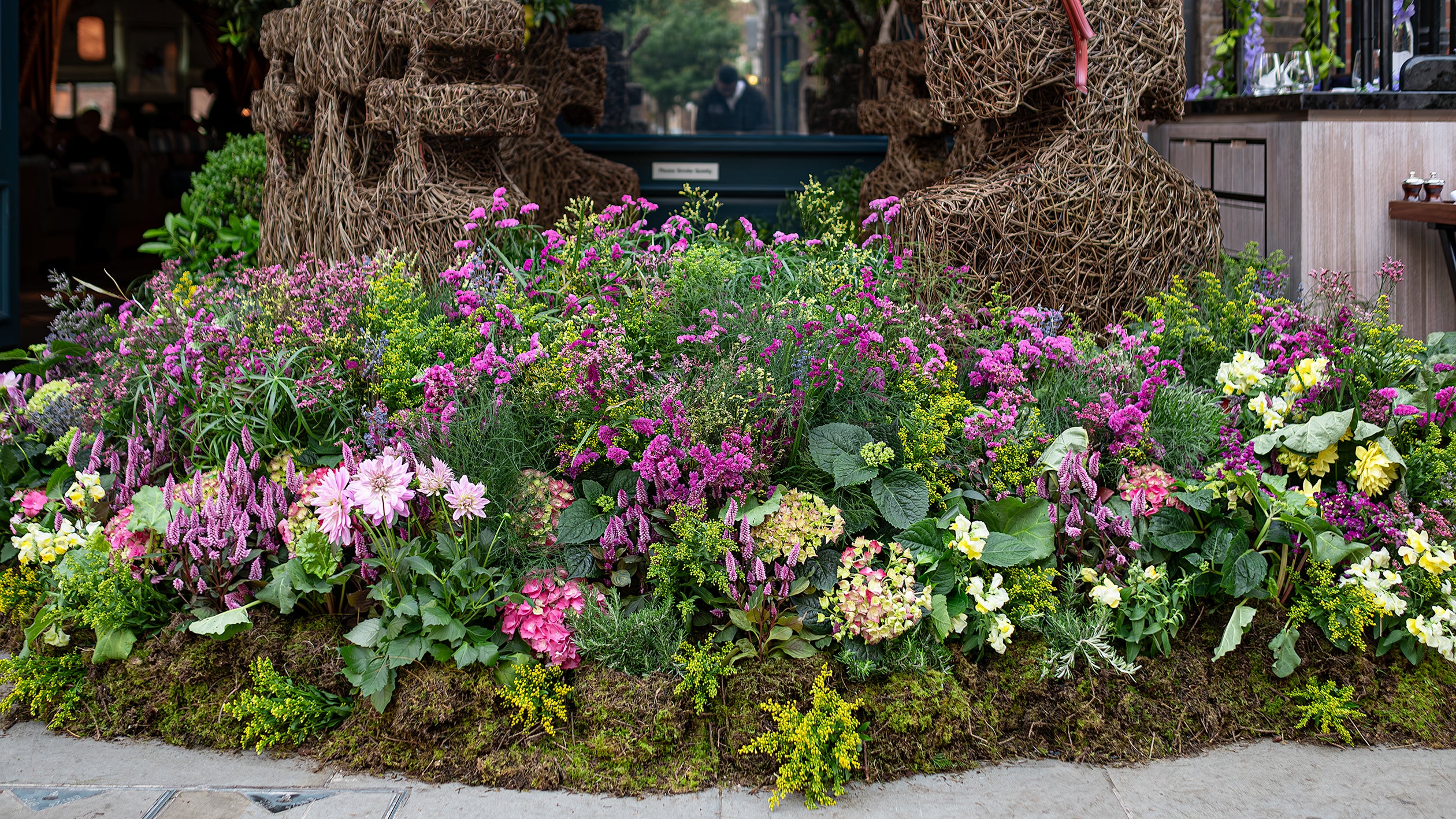 Close-up of a bespoke garden bed display at Chelsea in Bloom designed, created and installed by event florist Amaranté London, showcasing a variety of colourful flowers including pink dahlias, yellow chrysanthemums, and green hydrangeas.