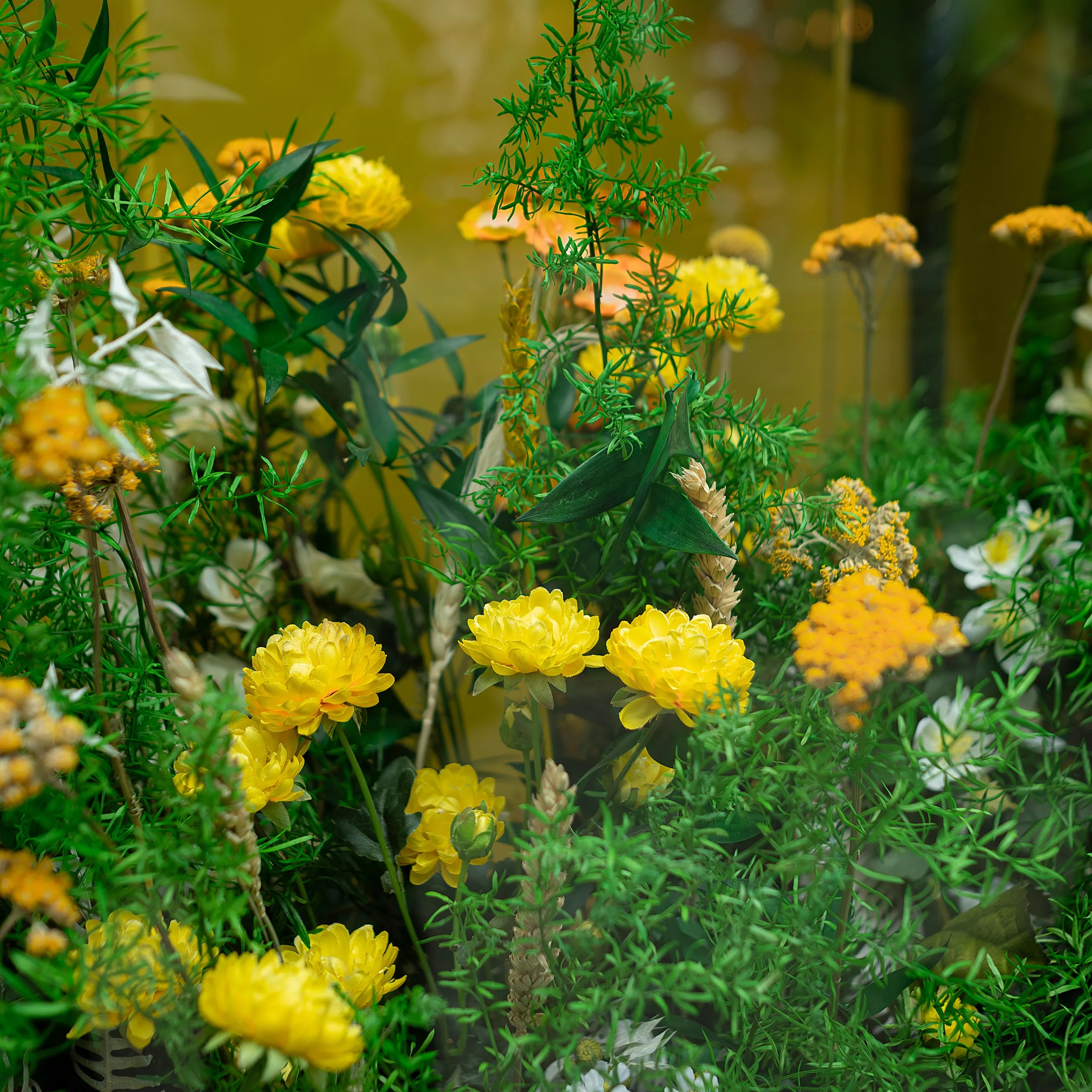 Detailed view of lush green foliage and yellow floral elements by Amaranté London for Beesou's window display at Amathus, Wardour Street, London. The floral arrangement adds a natural touch to the storefront, perfectly aligning with the brand's vibrant yellow colour scheme.