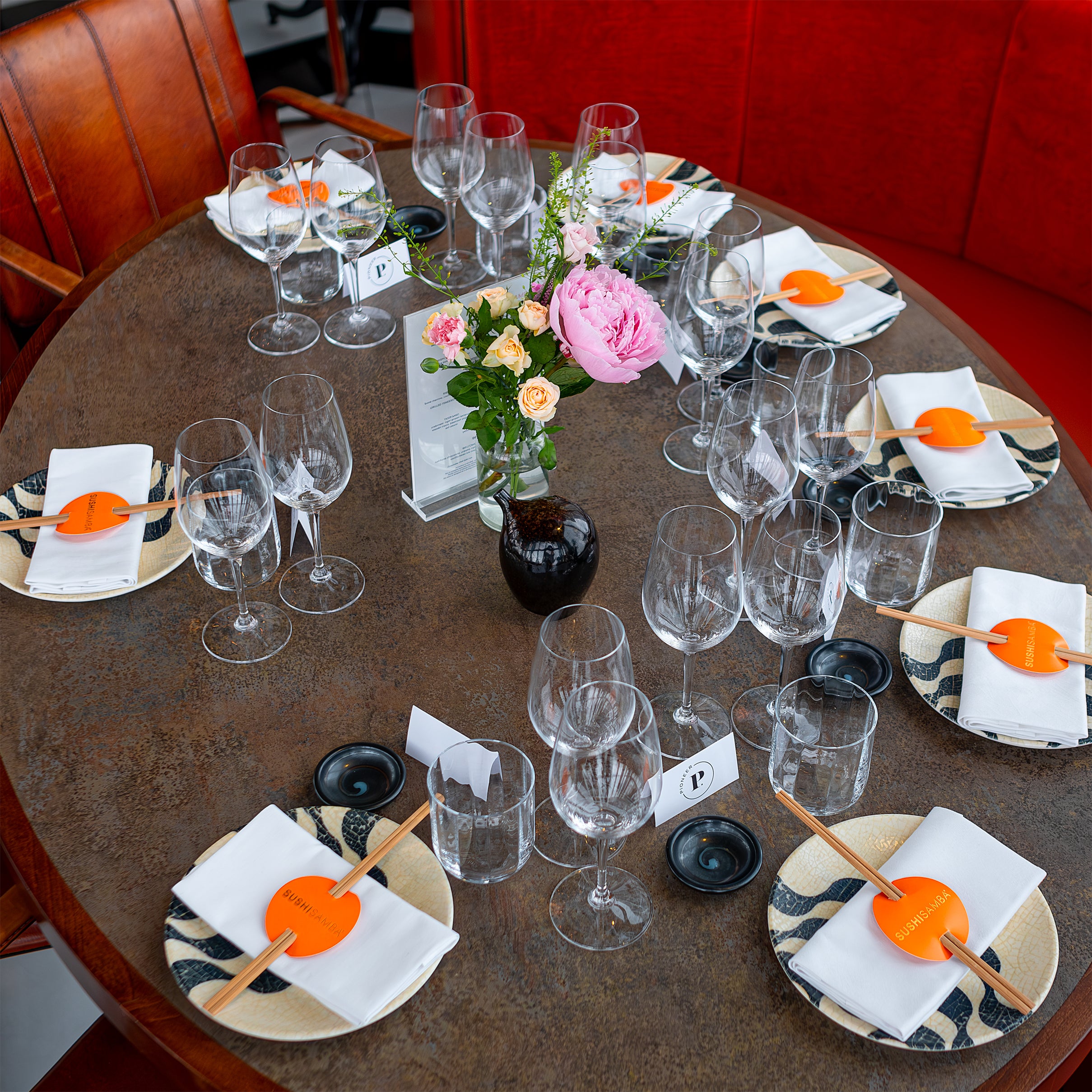 An elegantly decorated oval table set for a corporate event at SUSHISAMBA with floral arrangements by Amaranté London. The floral centrepiece includes pink peonies and roses, adding a touch of elegance and sophistication to the Chanel event.