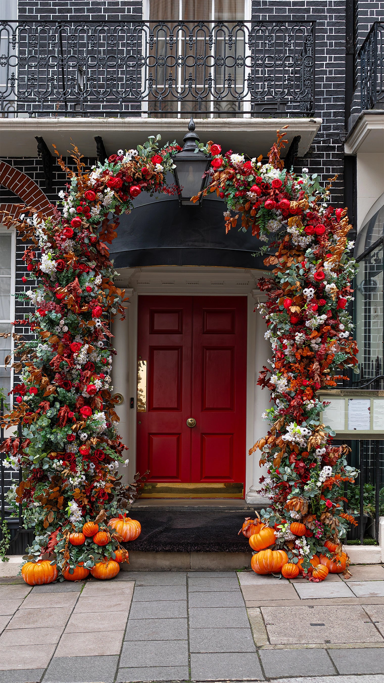 The frontal view of Amaranté London’s bespoke floral arch for The Crown London Members Club. It features red roses, autumn leaves, and delicate white flowers, and captures all the beauty of autumn colours.