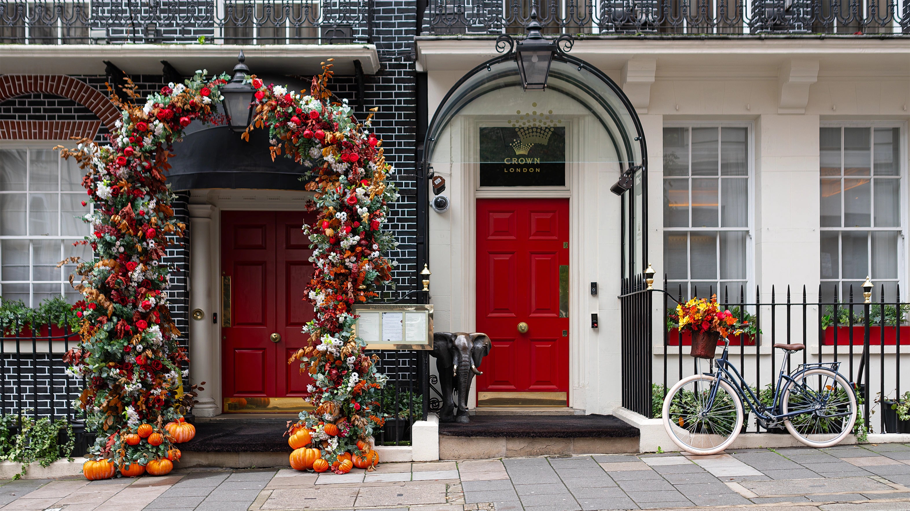 The frontal view of Amaranté London’s bespoke floral arch for The Crown London Members Club. It features red roses, autumn leaves, and delicate white flowers, and captures all the beauty of autumn colours.