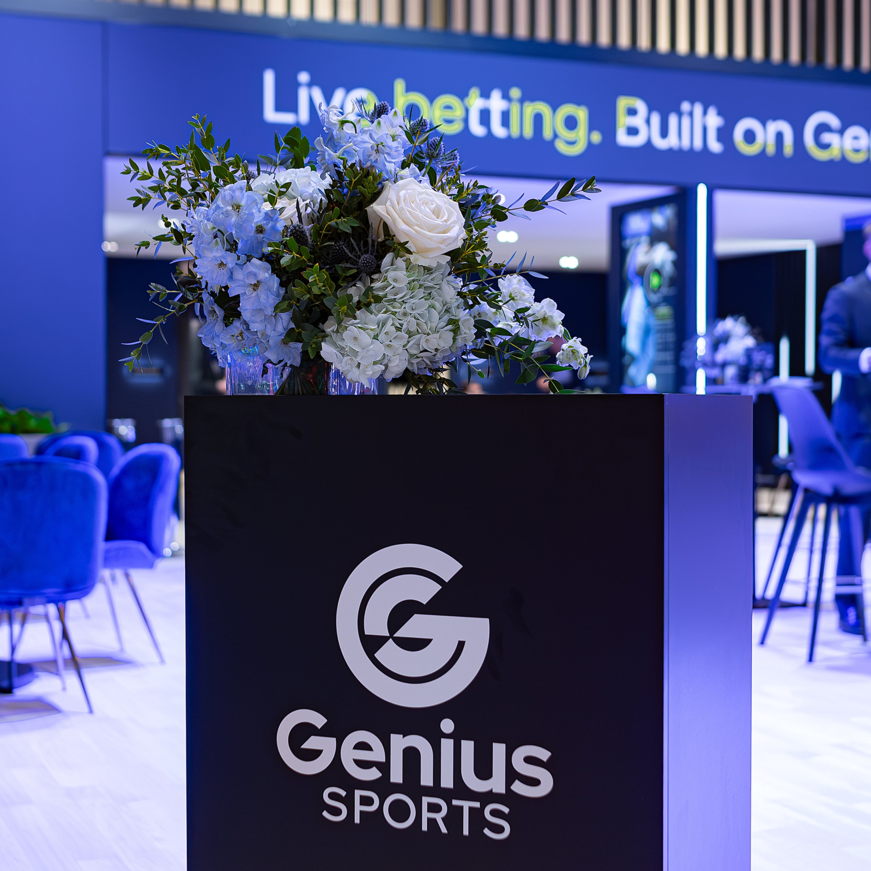 A luxury bouquet of white roses and hydrangeas atop a Genius Sports podium at The Genius Sports Booth decorated with Amaranté London bespoke floral installations