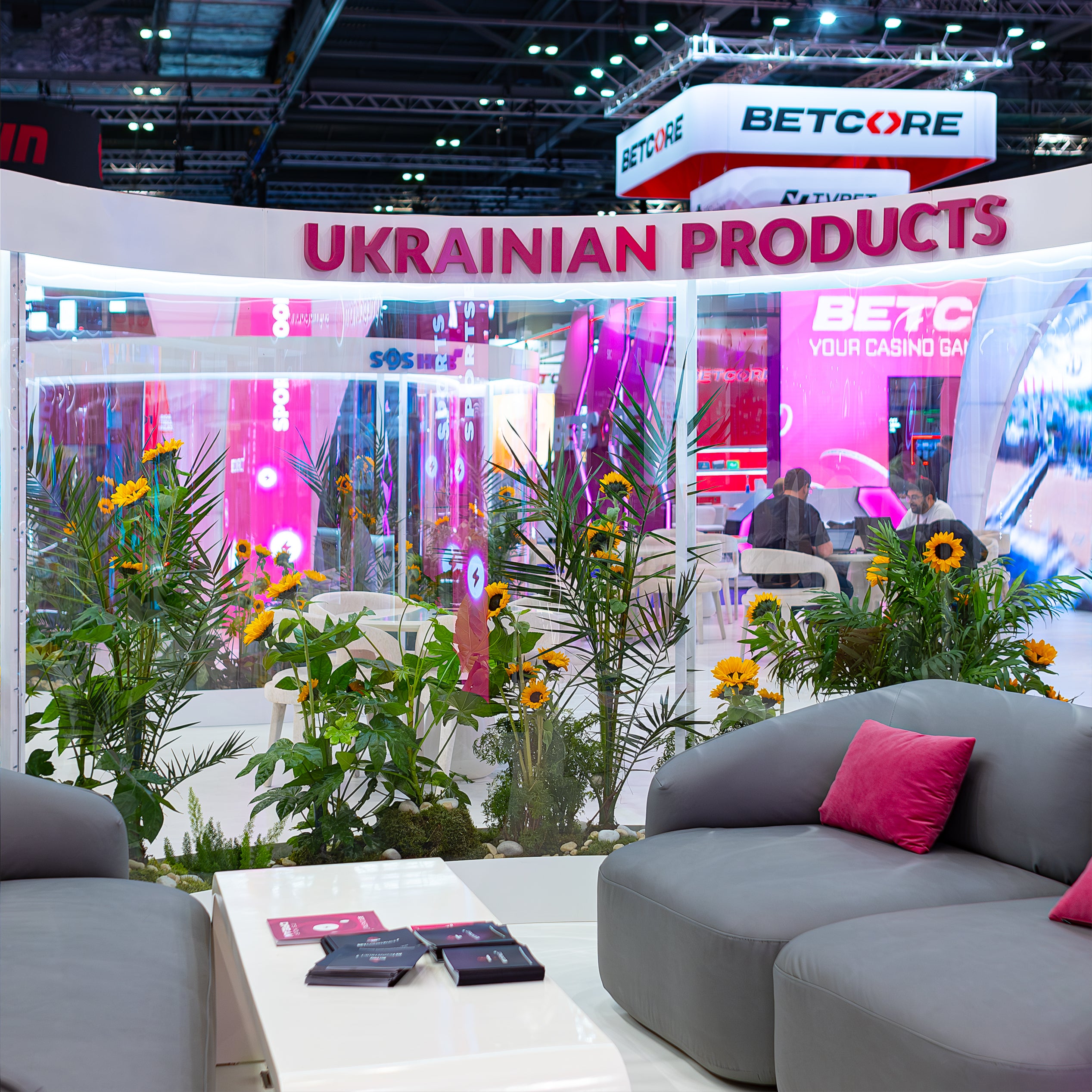 Stand with Ukrainian products branding in the background at the ICE London Exhibition decorated with a cheerful arrangement of sunflowers designed and produce by Amaranté Event Florist in London