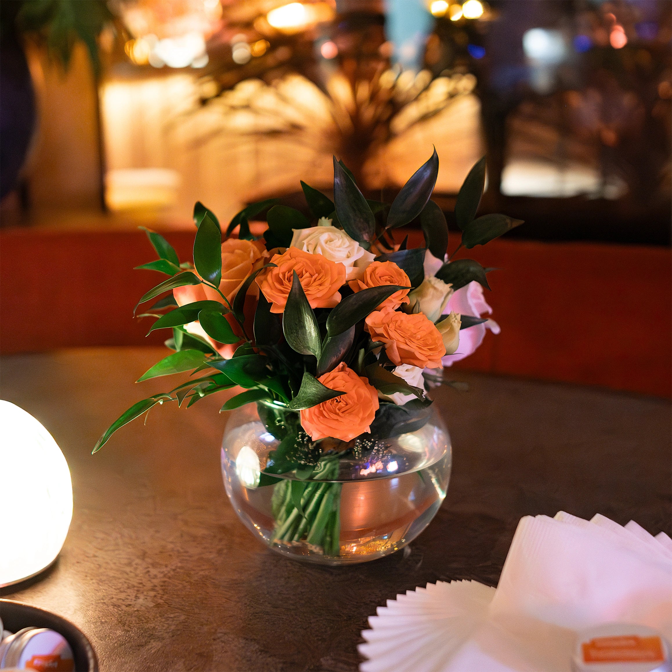 A sophisticated floral arrangement with vibrant orange and cream roses accented by lush greenery elevates the decor at the EasyJet annual partner event in London - Floral Design By AmarantÃ© London