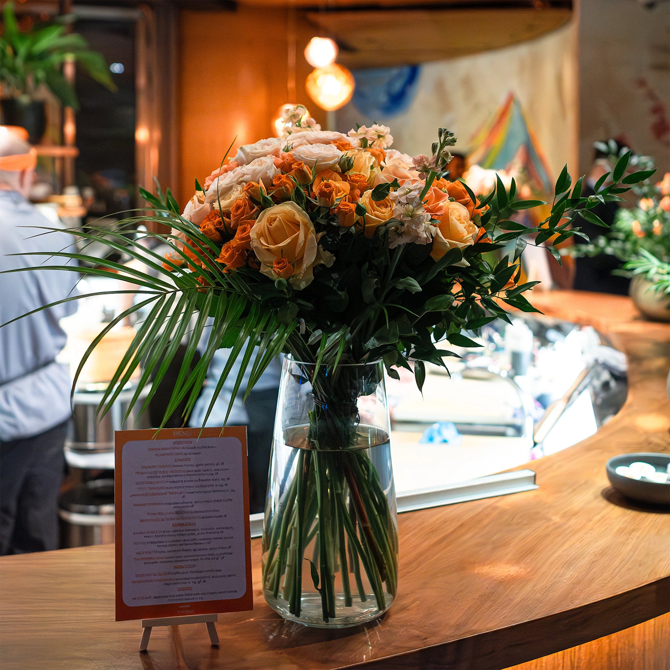 A rich bouquet with pink and orange roses, pink lisianthus and eucalyptus leaves, illuminated by dim candlelight, creates an intimate and elegant atmosphere at the EasyJet event at SushiSamba.