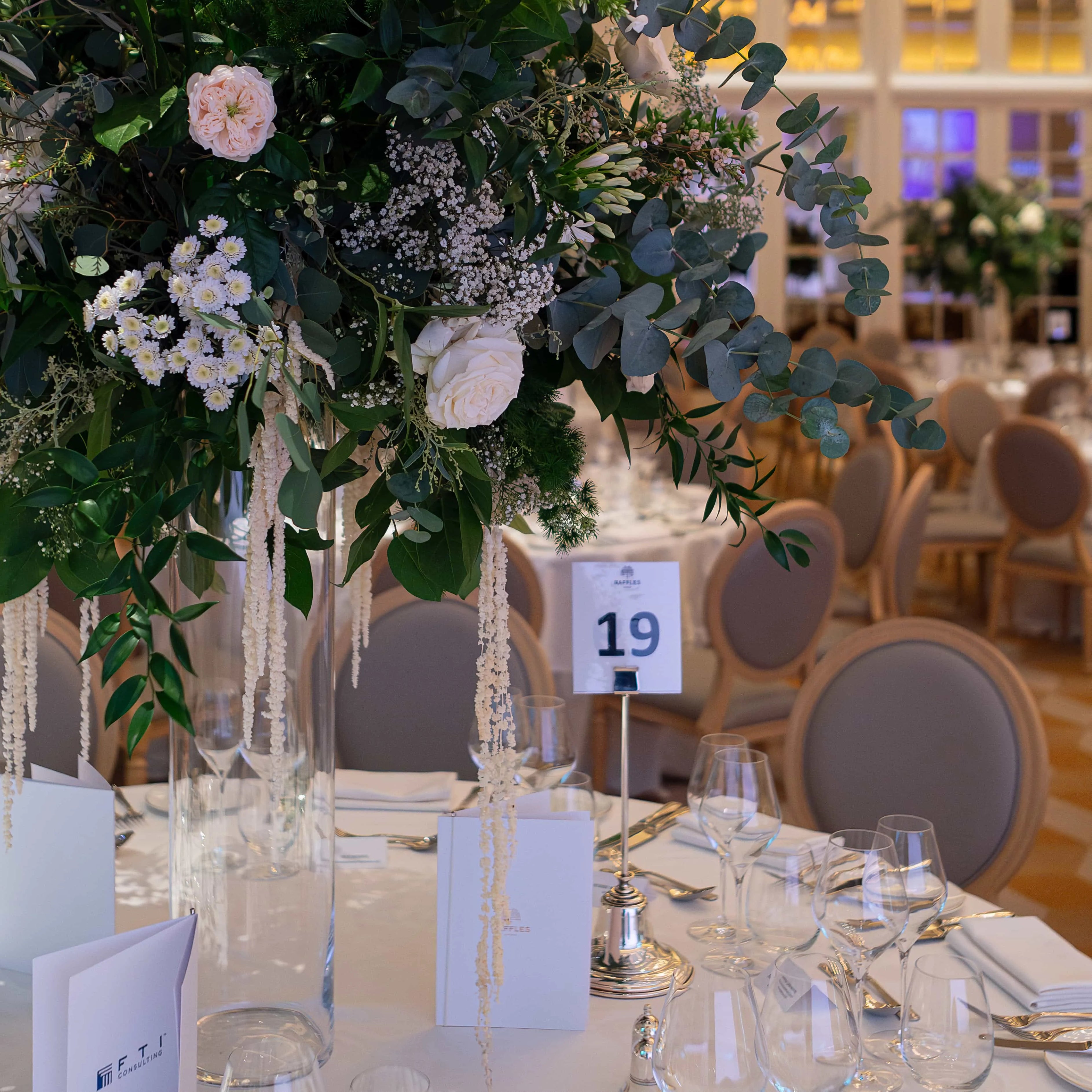 This is a photo of an exquisite floral arrangement by Amaranté London on a table at the FTI Consulting corporate event. The arrangement features delicate roses and cascading greens, with dangling accents adding a touch of luxury and whimsical sophistication.