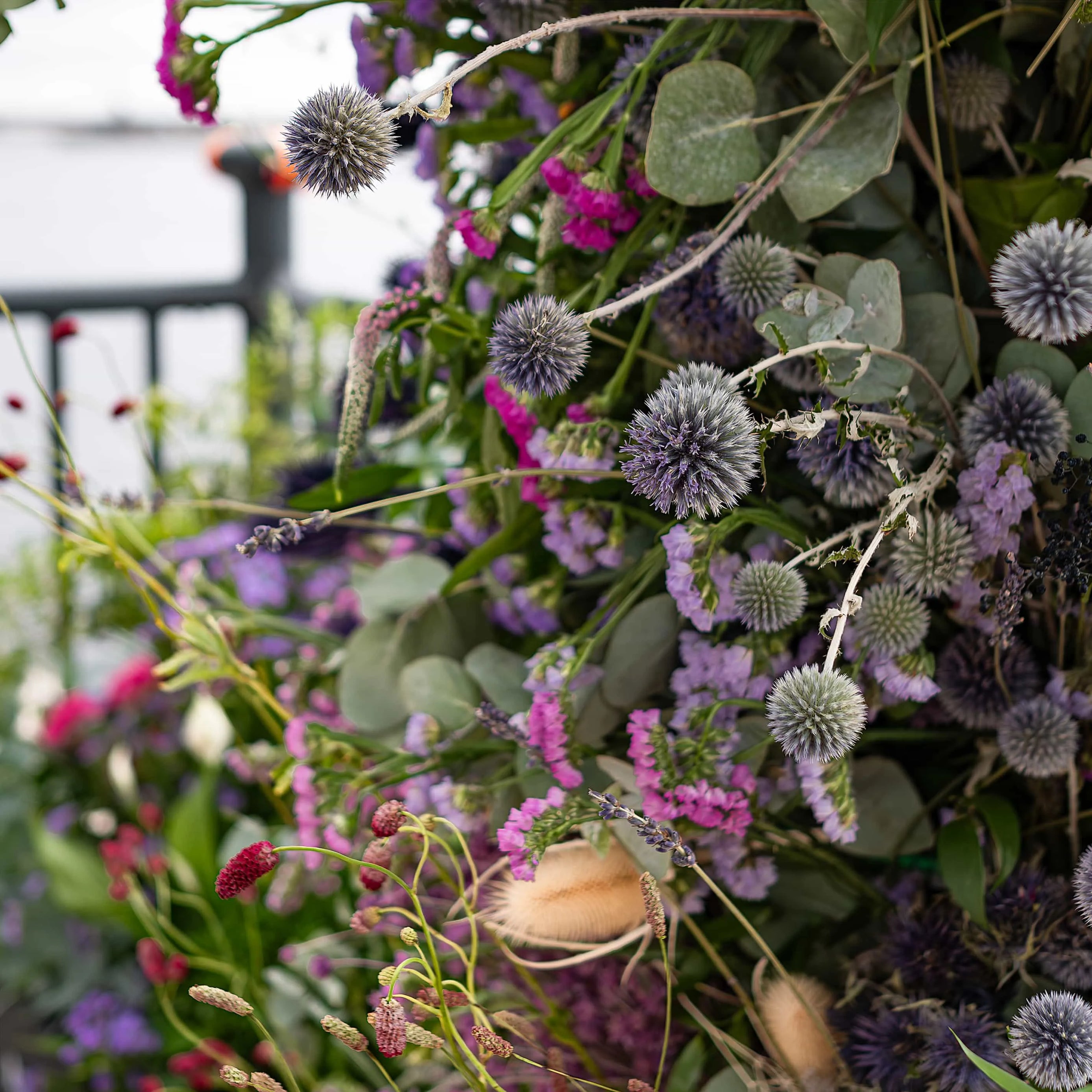 This is a close-up of a rich and colourful floral arrangement at the Formula E event. It features spherical purple thistles, delicate pink blooms, and textured foliage, artistically assembled to evoke a sense of natural beauty and sophistication - Amaranté London.