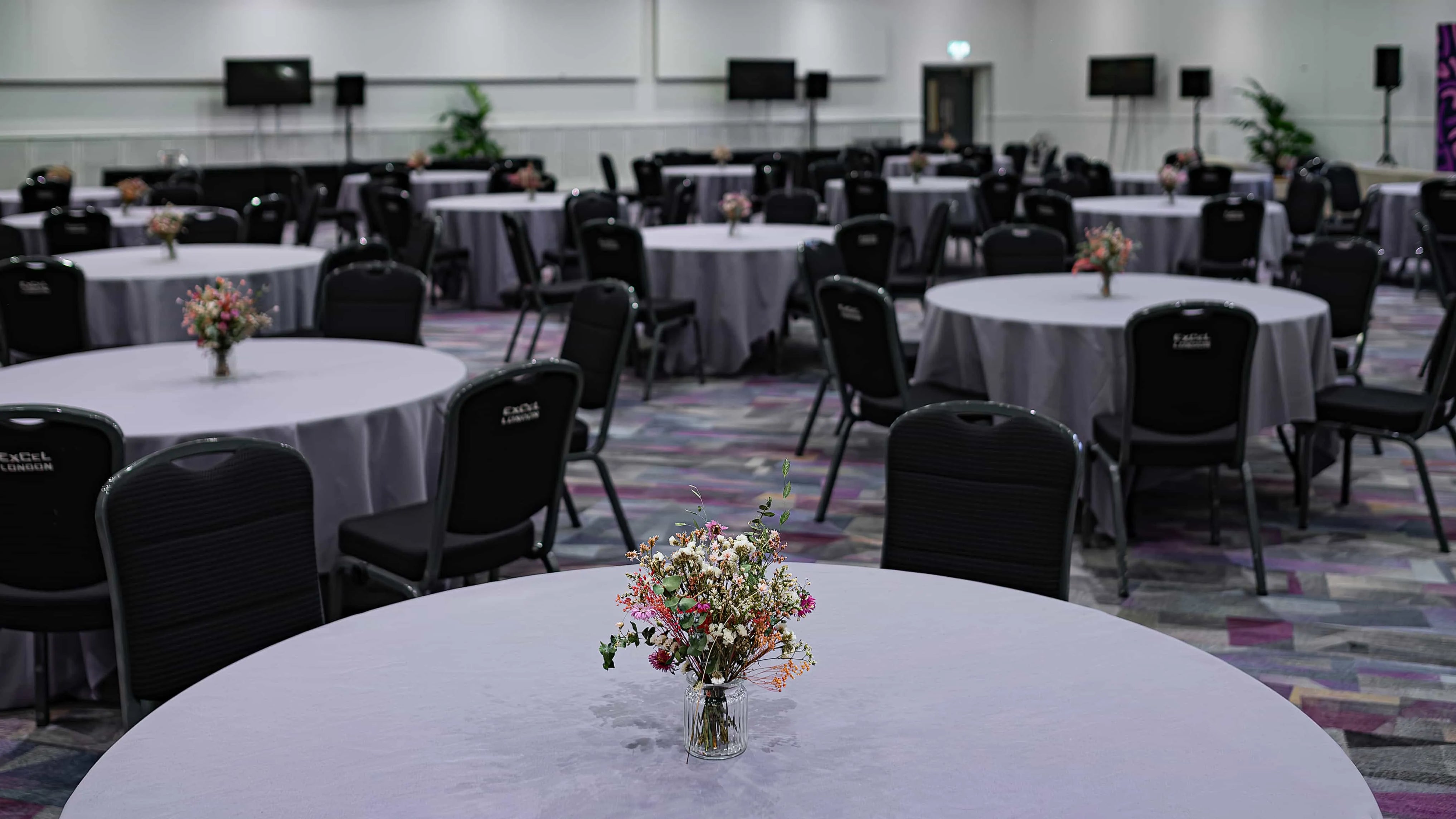 Corporate conference setting with simple yet elegant floral centrepieces on tables, providing a subtle yet sophisticated ambience for the Formula E event at the Excel Centre - Amaranté London.