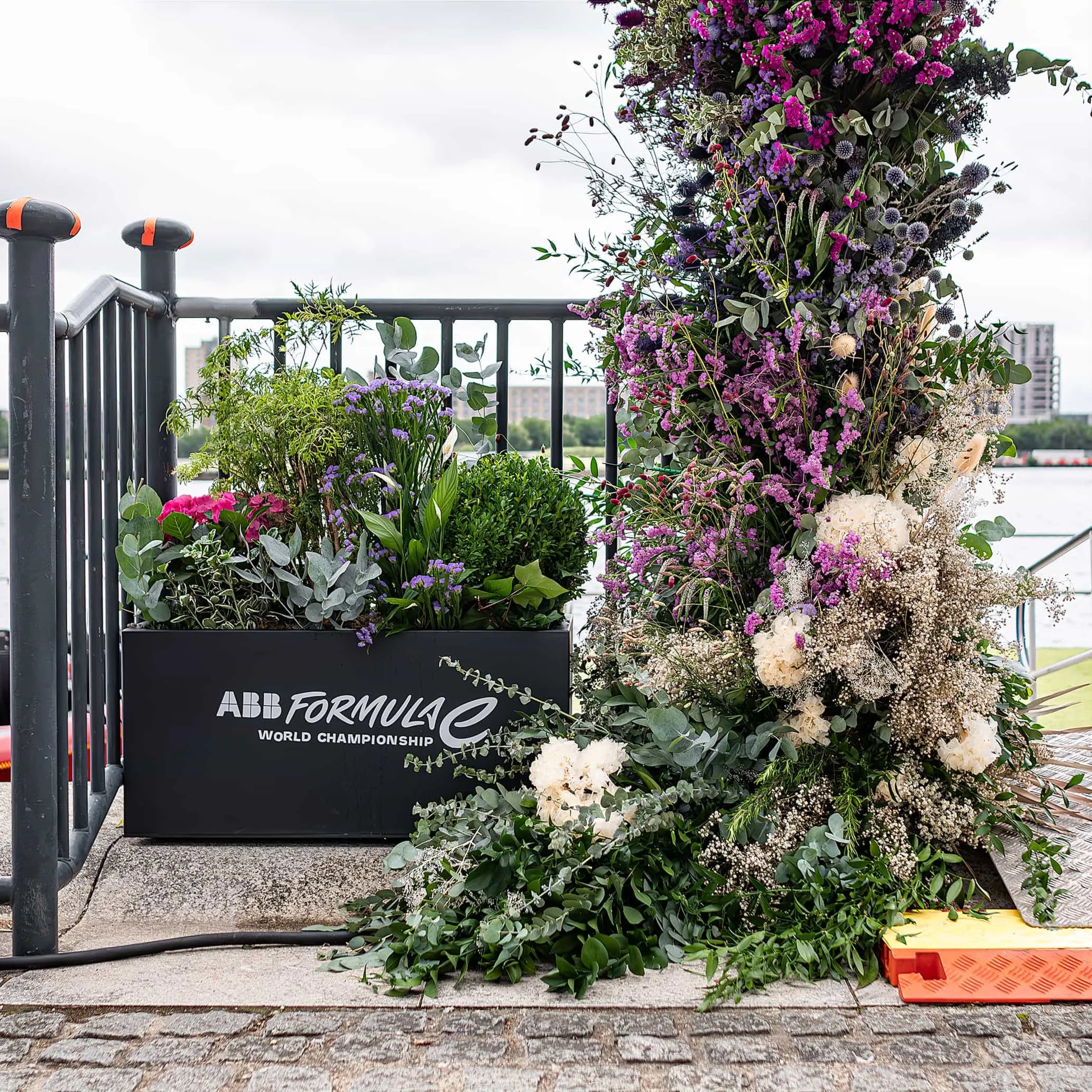 A luxurious and vibrant floral display featuring a mix of purple, pink, and white flowers elegantly adorns the event entrance at the ABB Formula E World Championship in London — Event Floristry by Amaranté London.