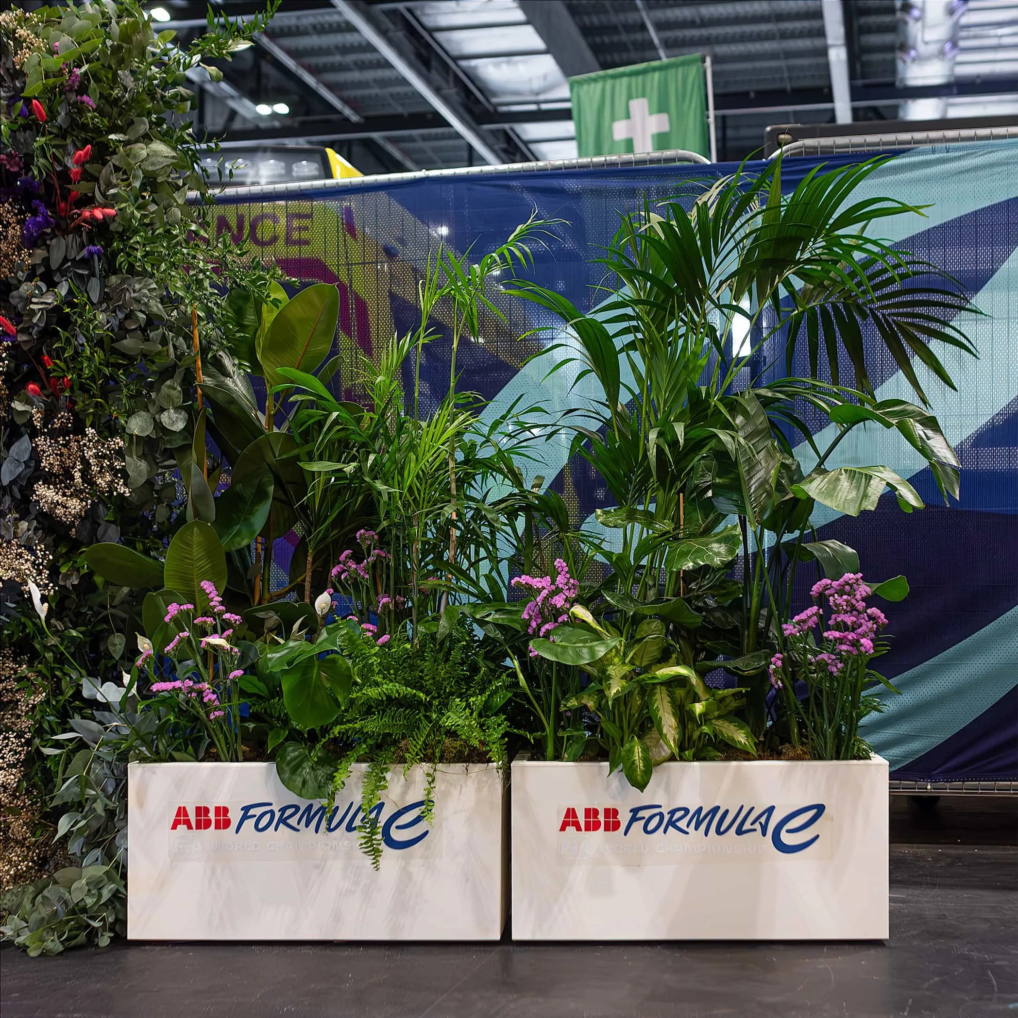 An extensive indoor plant installation—planters at the Formula E venue—showcases a variety of lush green plants and pink blooms. Plant hire turnkey service by Amaranté London.