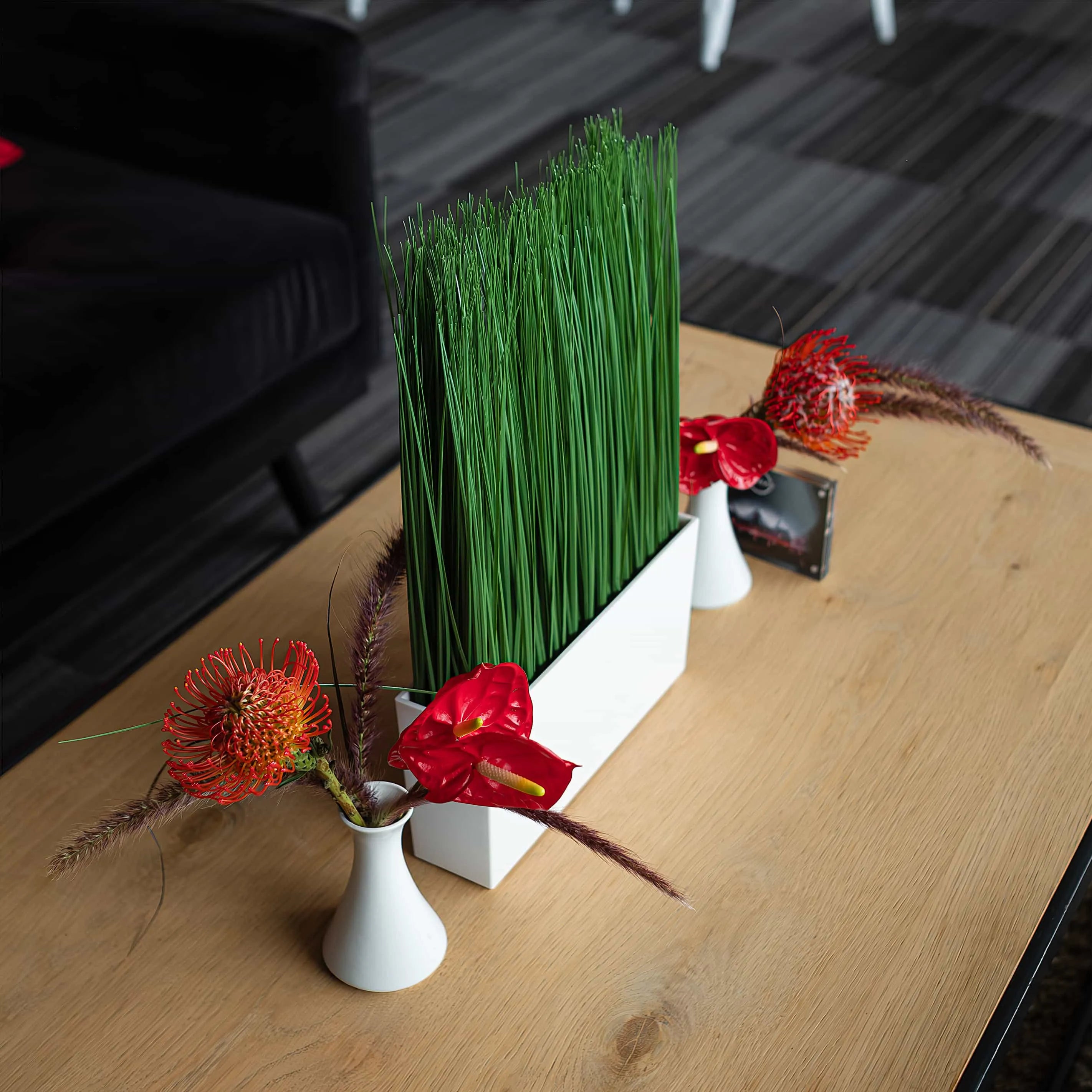 Amaranté London's innovative greenery installation, presenting tall grasses and vibrant red floral accents in minimalist vases on a wooden table, illustrating a fusion of nature and modern design at the Formula E Word Championship Event, in the lounge area.