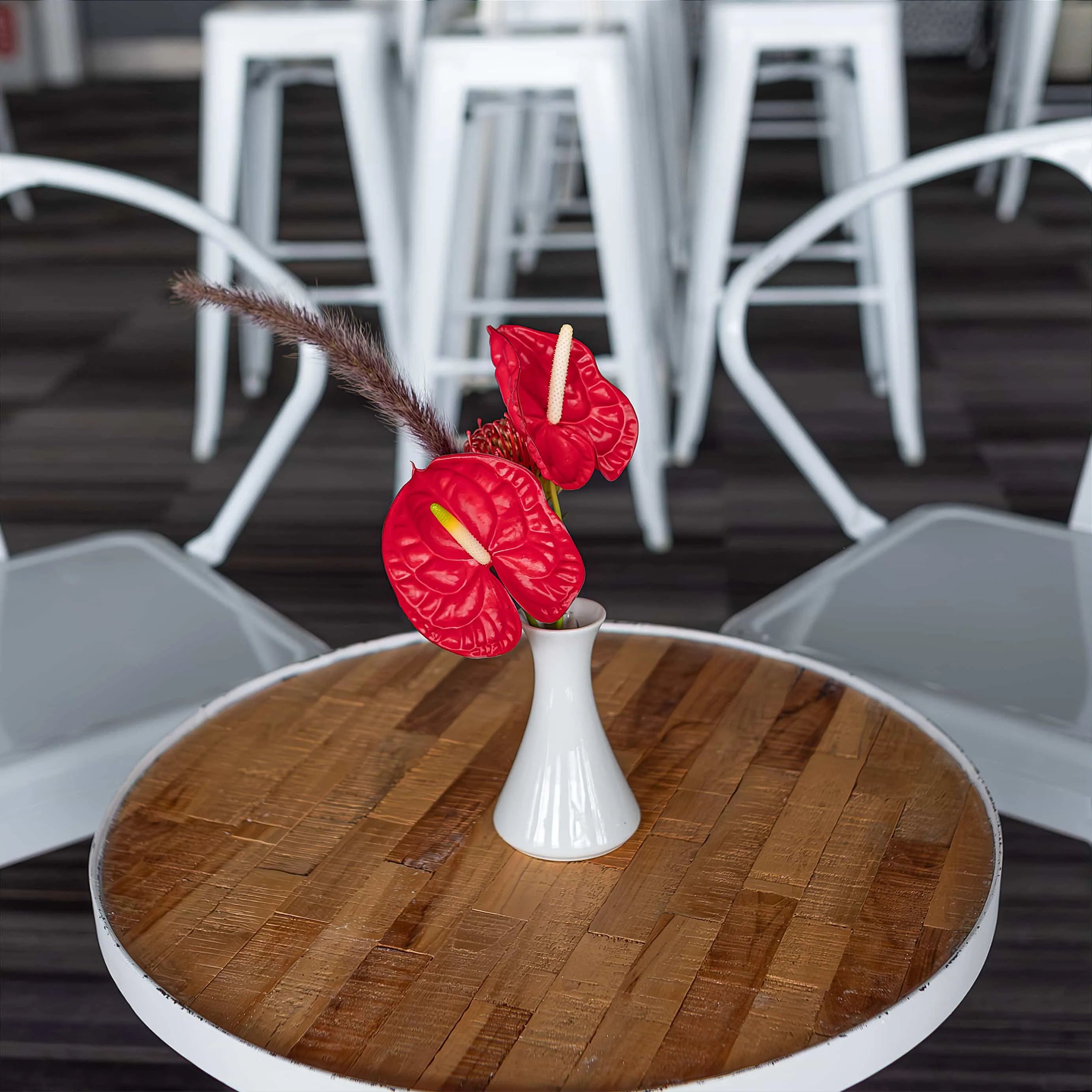 Vibrant table centerpiece by Amaranté London featuring red anthuriums and exotic feathers in a sleek white vase, set in a contemporary white-themed Formula E lounge, symbolising energy and passion - Amaranté London, Event Florist.