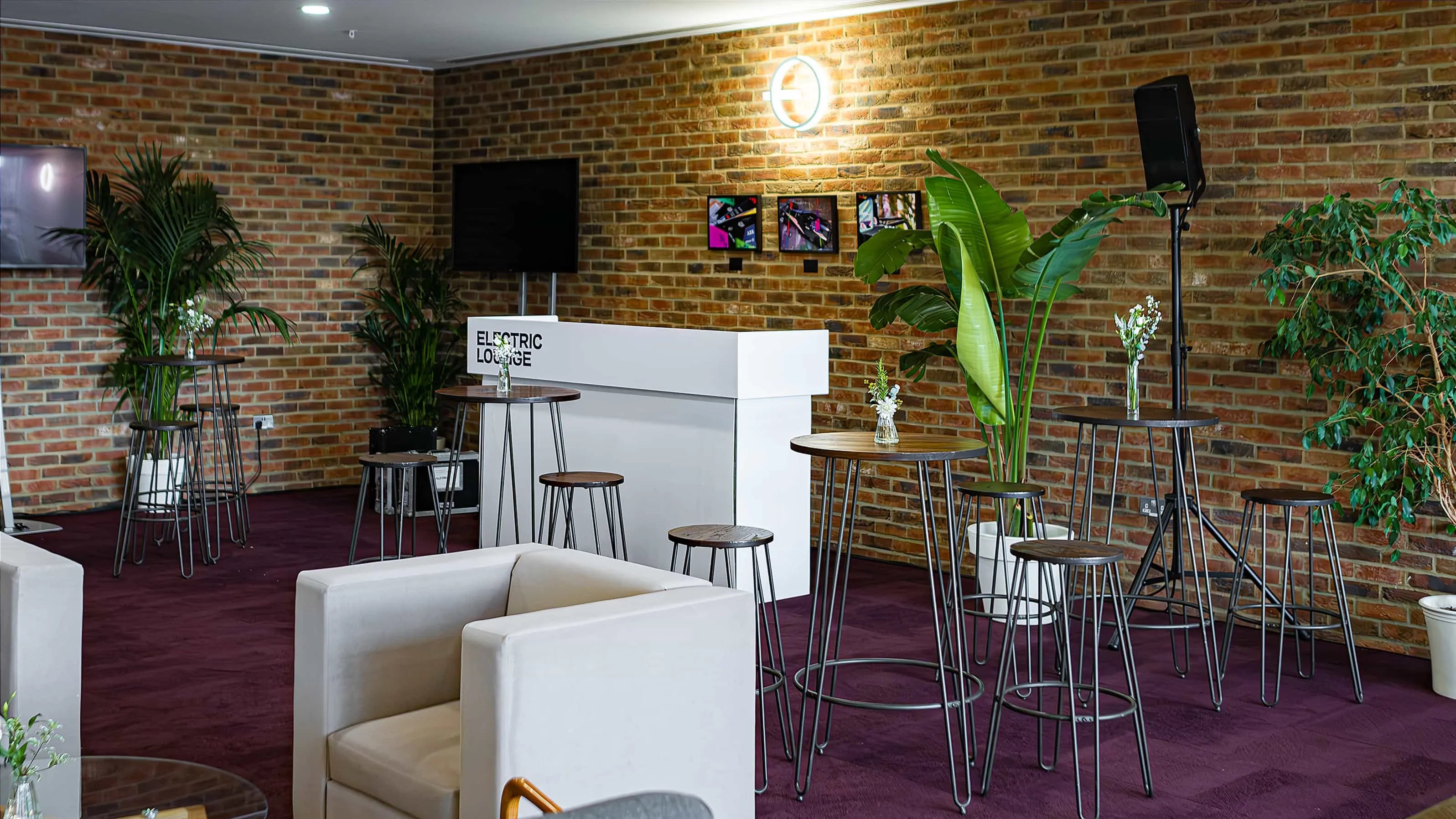 Spacious lounge setup at the Formula E event with stylish brick walls adorned with stylish planters featuring bright green plants and small floral arrangements - Amaranté London, Event Florist in London
