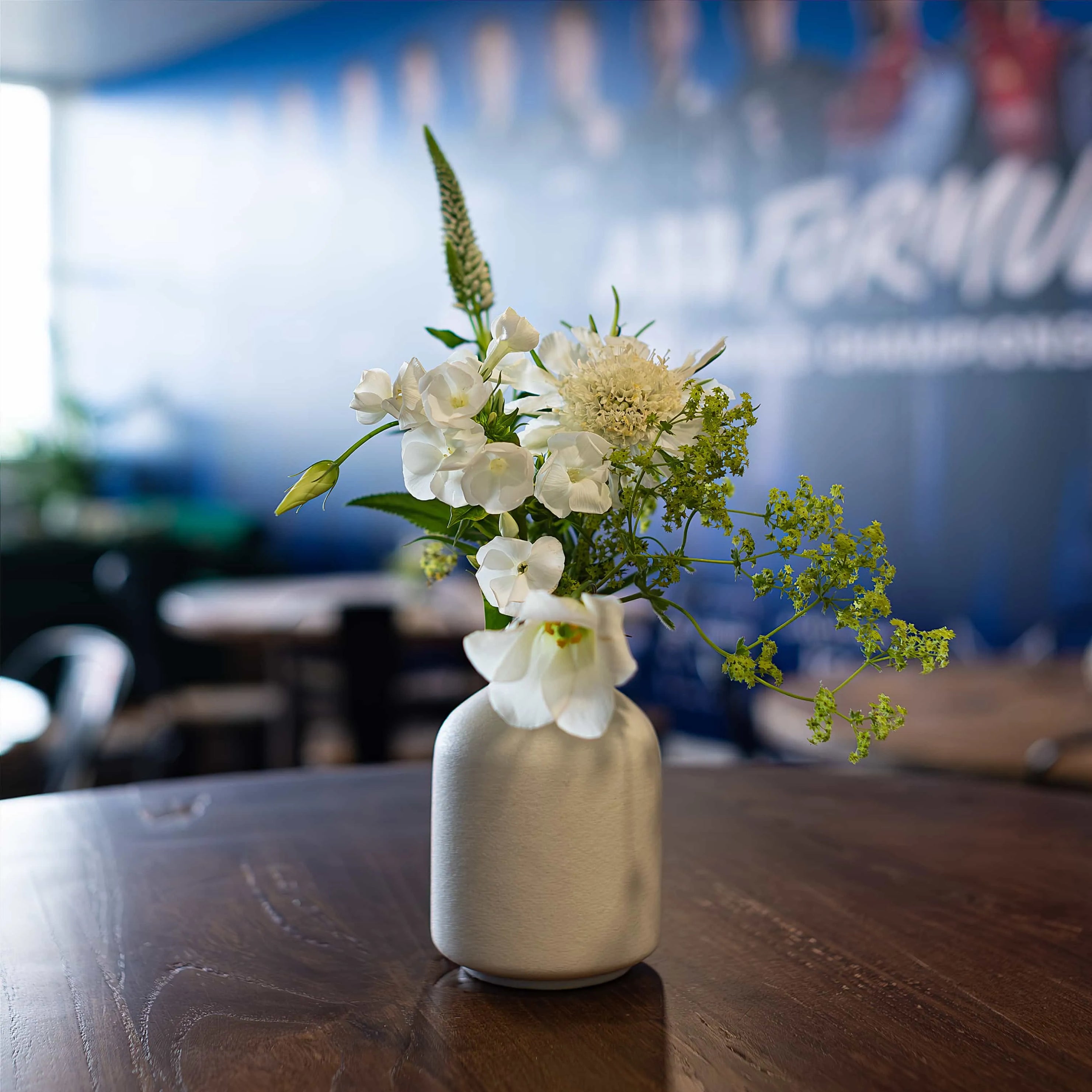 Amaranté London's delicate floral arrangement in a modern white vase featuring white orchids and green foliage, set against the backdrop of the Formula E branding.