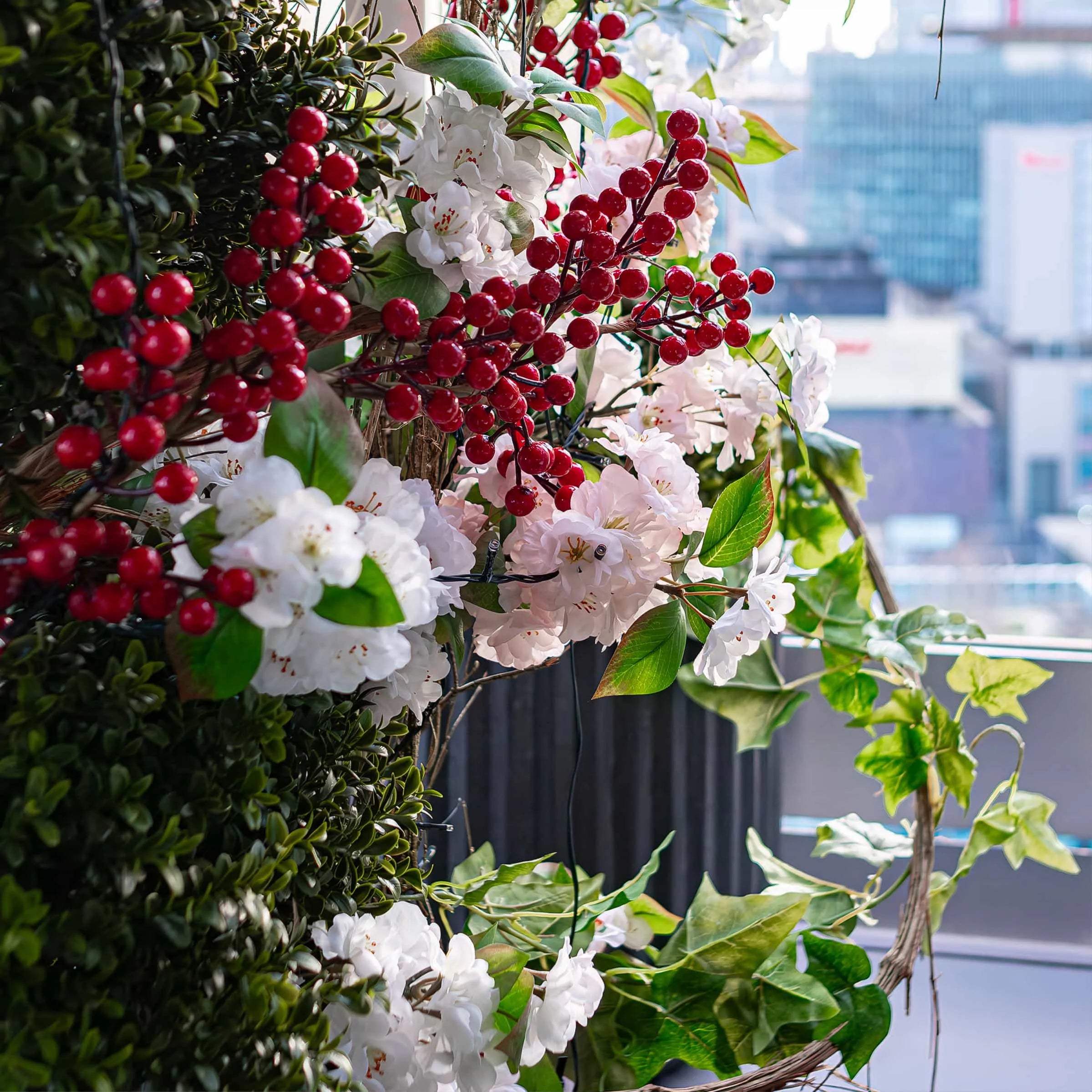 A close-up of a Christmas floral decoration for a window, set against an urban backdrop visible from the rooftop of STK Steakhouse - Amaranté London, Event Florist
