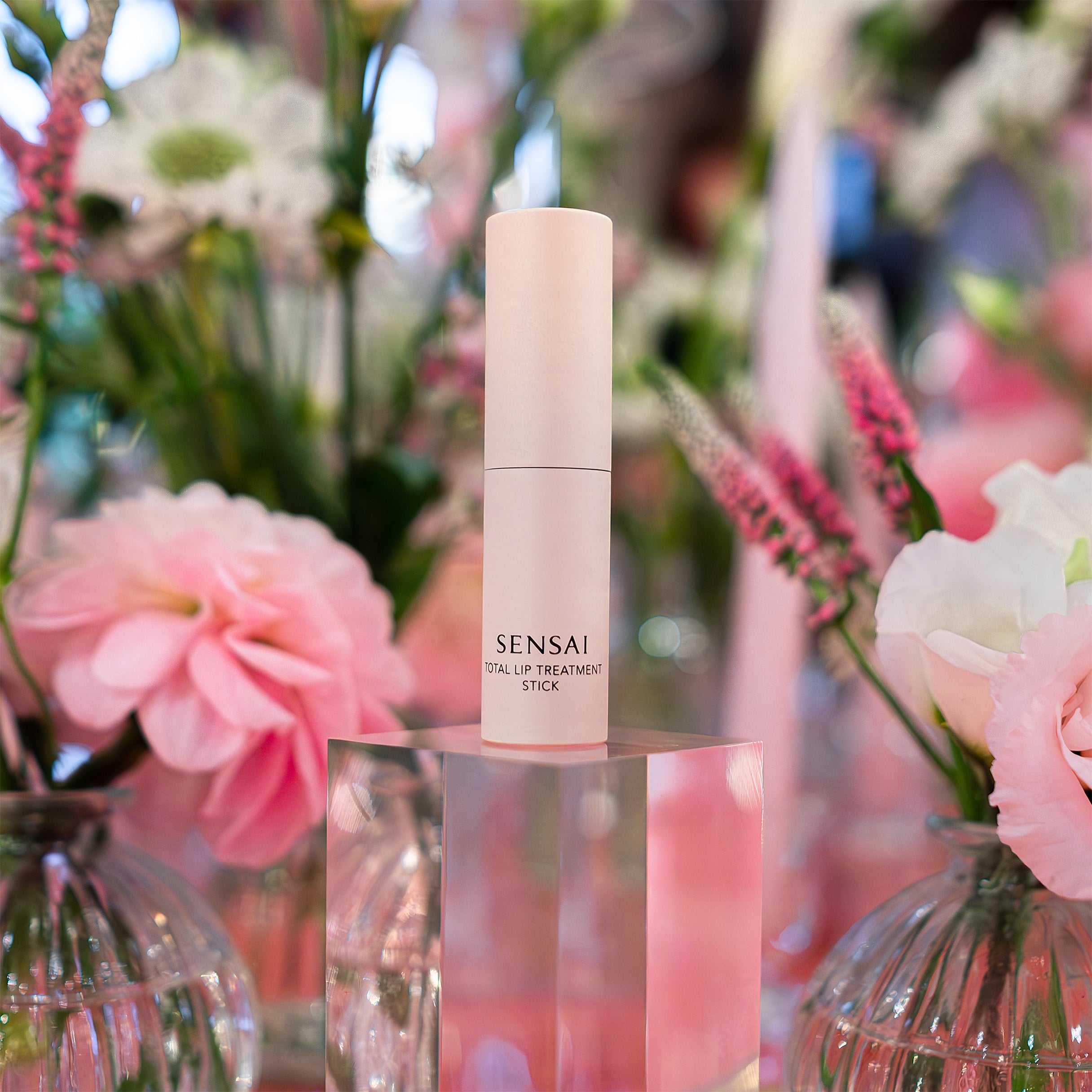 Sensai Total Lip Treatment Stick is elegantly displayed among pink and white floral arrangements by Amarante London, adding a touch of luxury to the Sensai product launch in London.