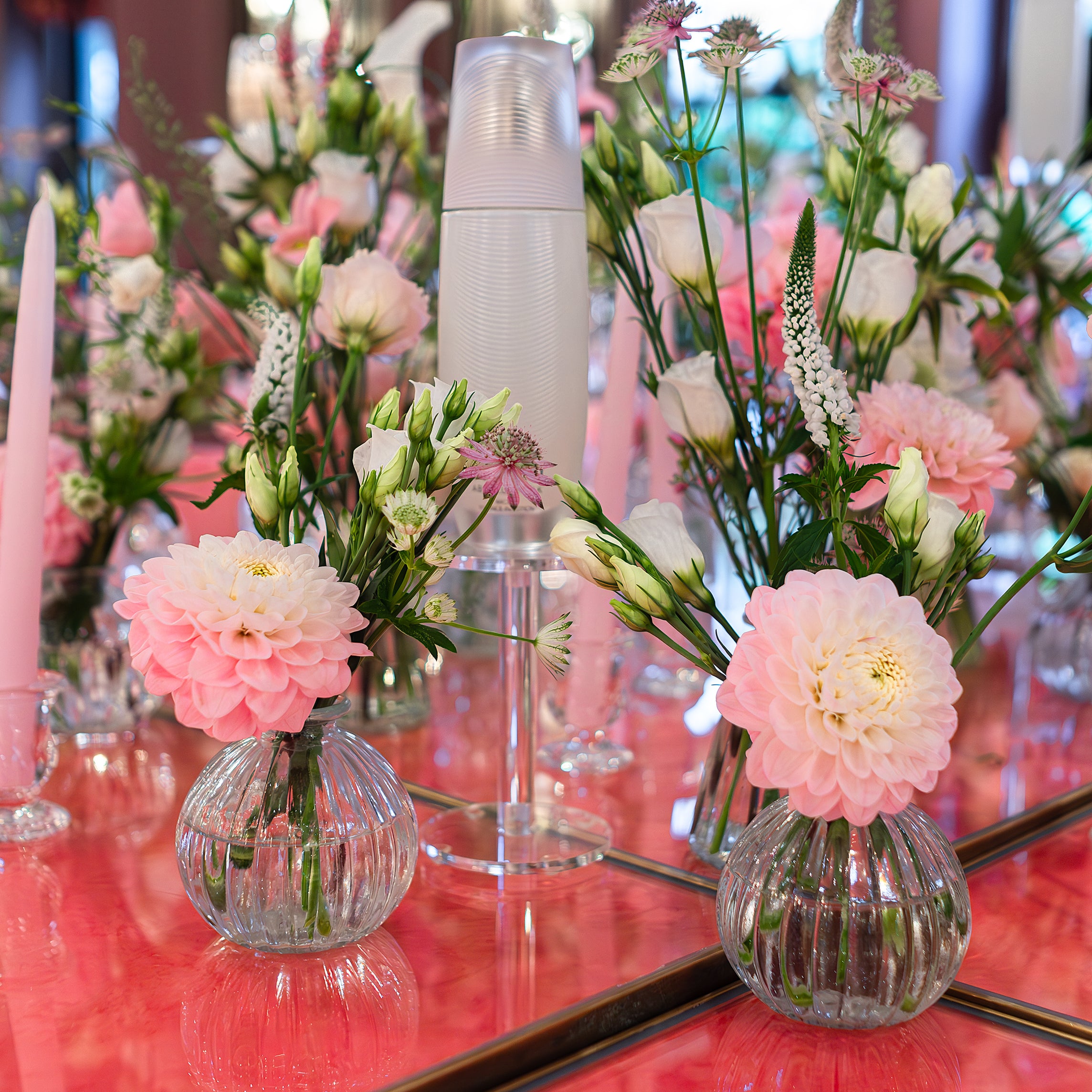 Delicate pink and white floral arrangements by Amarante London for the Sensai product launch, displayed in clear glass vases on a mirrored surface, enhancing the elegance of he location (Beaverbrook Town House).