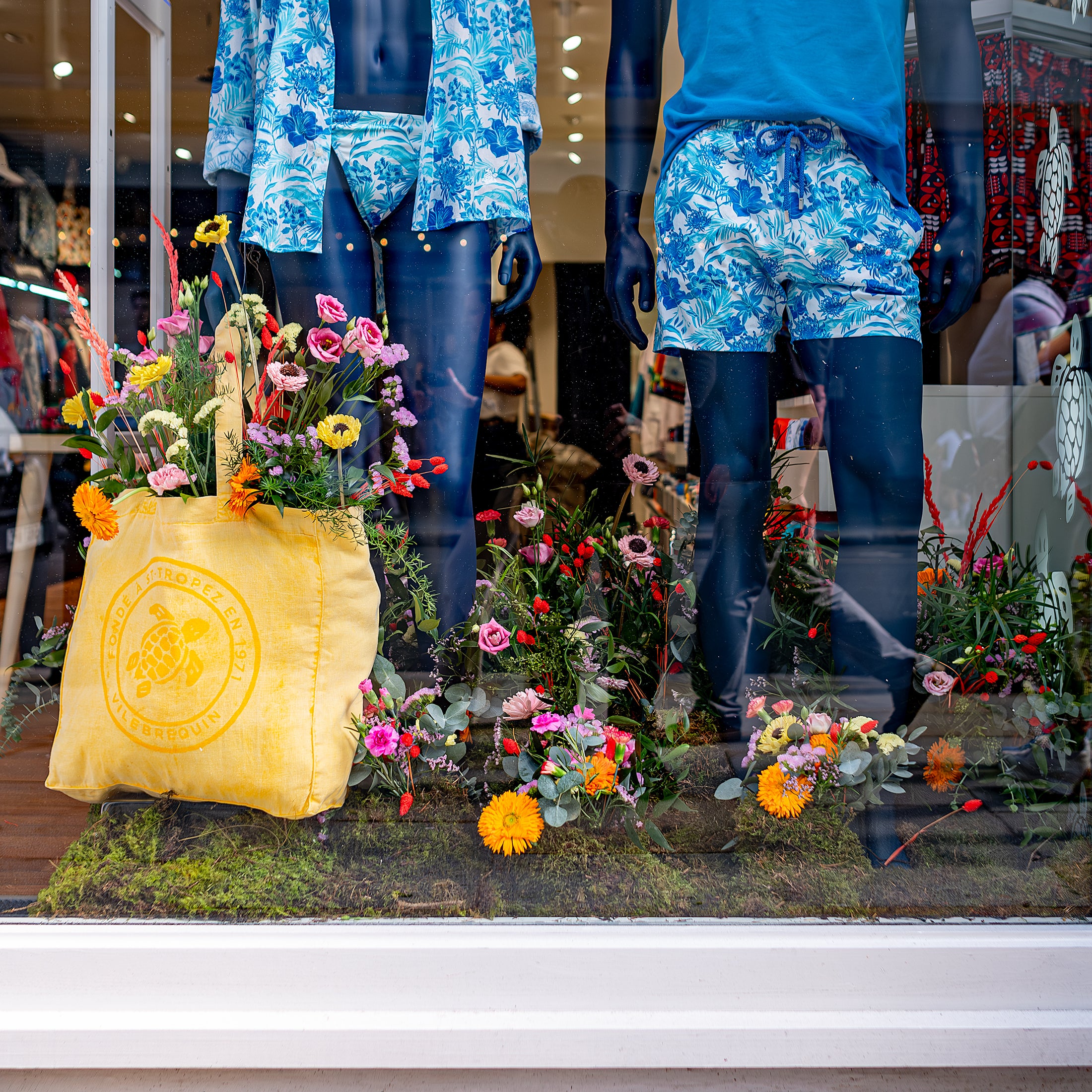 Vilebrequin store window beautifully decorated with colourful floral arrangements by Amaranté London for Chelsea in Bloom, featuring mannequins dressed in swimwear and lush greenery at the base - Amaranté London, Event Florist