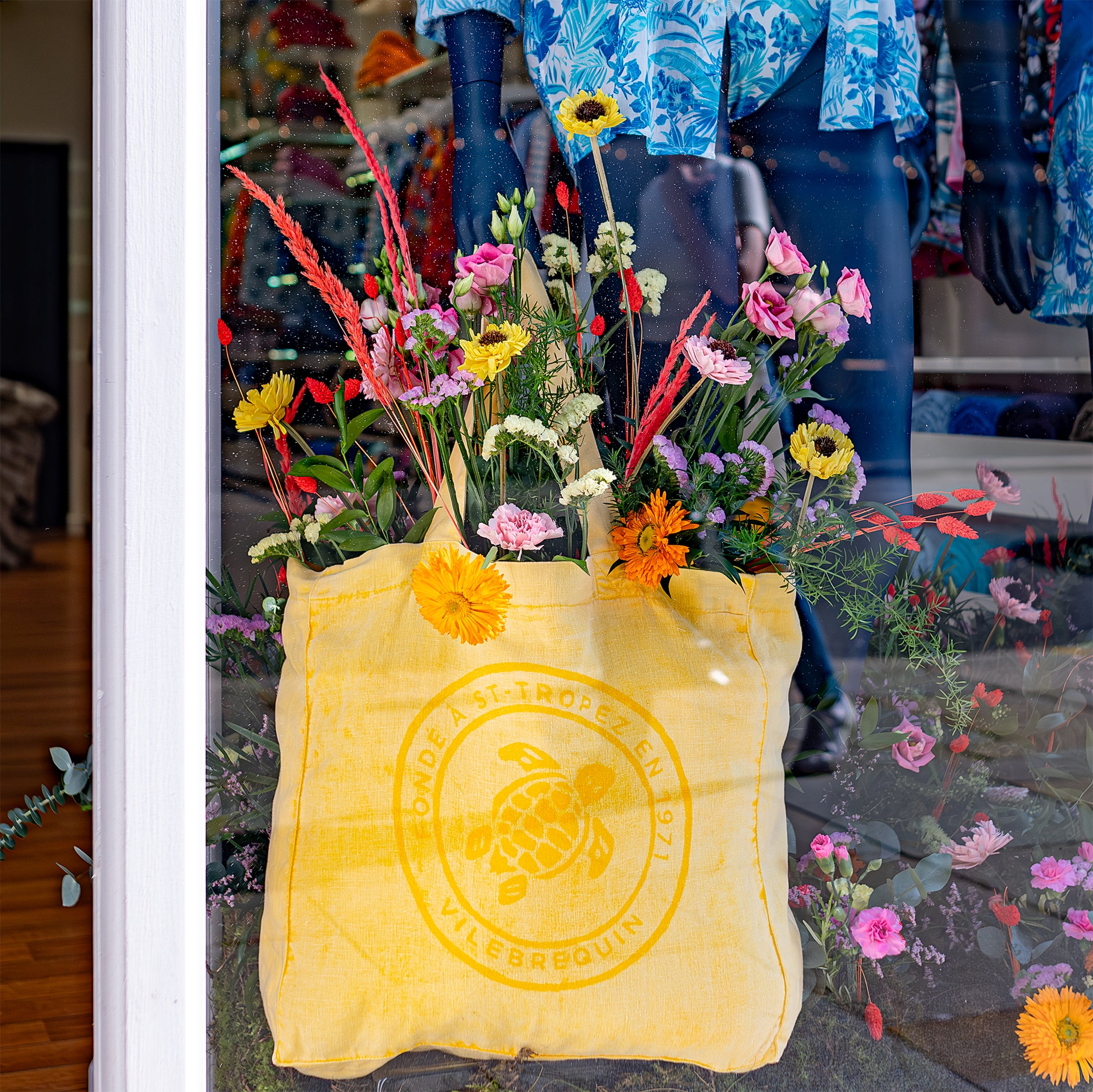 A close-up of a yellow tote bag filled with vibrant flowers designed and installed by Event Florist Amaranté London, displayed at Vilebrequin for Chelsea in Bloom, complementing the luxurious and artistic ambience of the storefront.