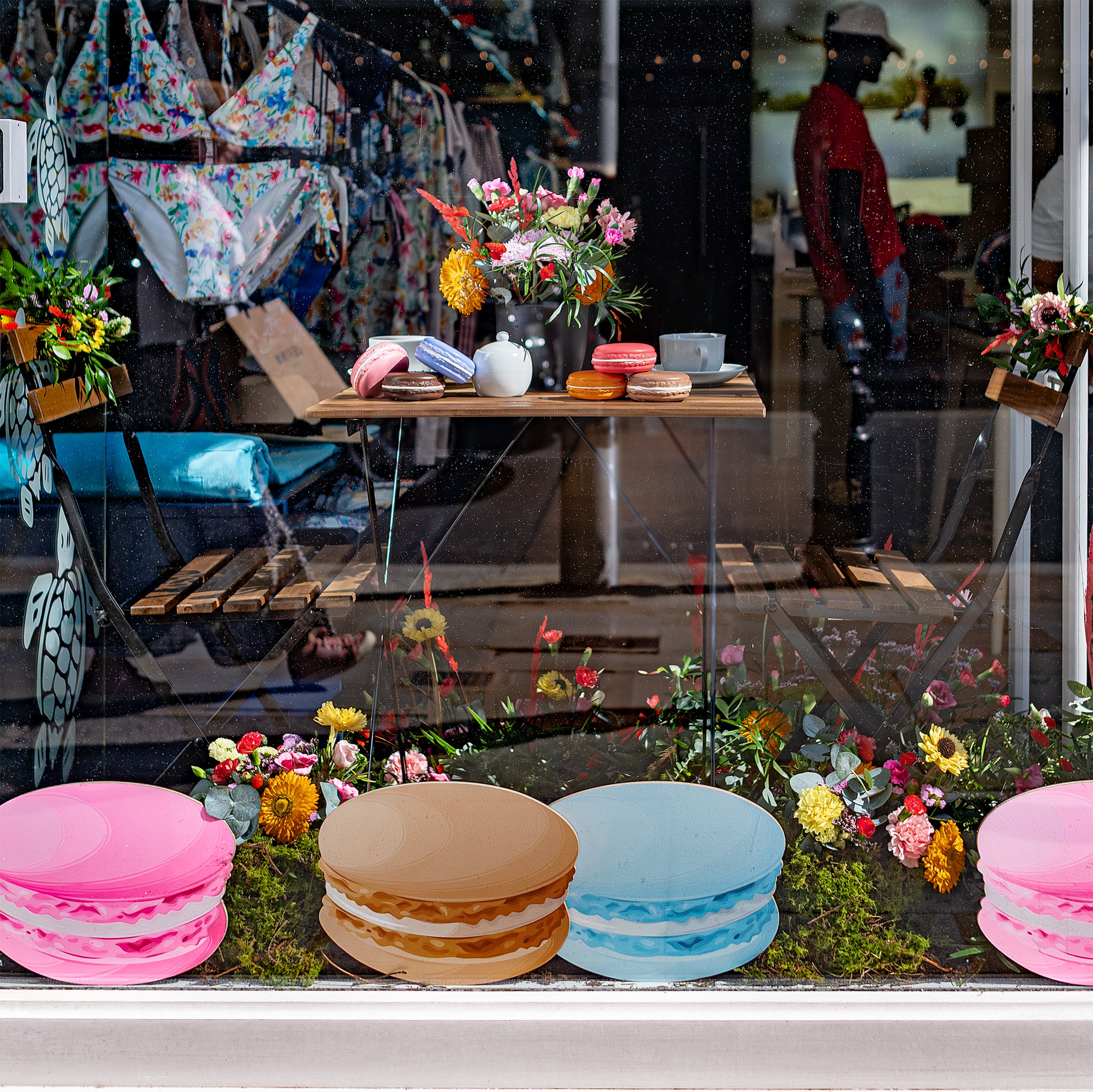 Vilebrequin store window decorated for Chelsea in Bloom with a charming bouquet of flowers designed by Amaranté London, featuring colourful flowers and a table with macarons, highlighting the vibrant atmosphere of the event.