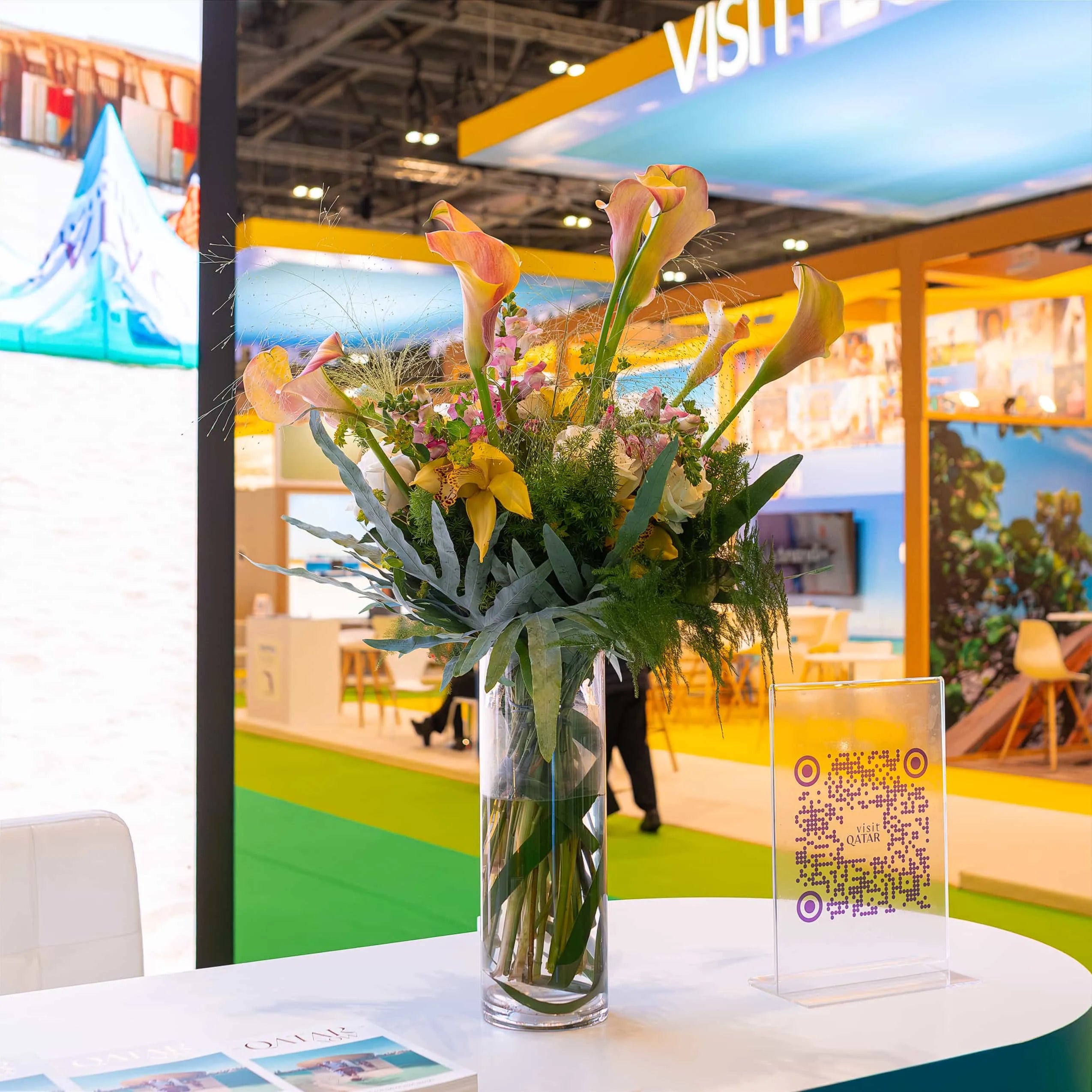 Amaranté London’s captivating tall calla lily arrangement at WTM is an elegant addition to this booth, which is in a bright event space area.